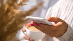 A woman looking at her phone with a coffee in her other hand